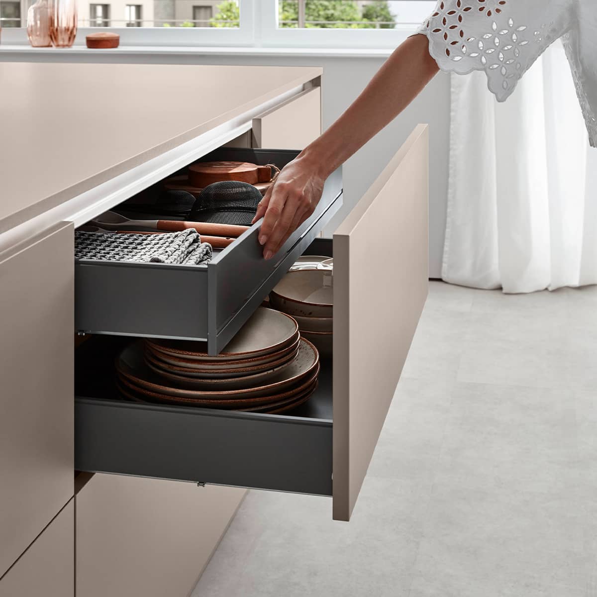 Close-up of a kitchen drawer system showing neatly organized utensils above and stacked dishes in a lower drawer.