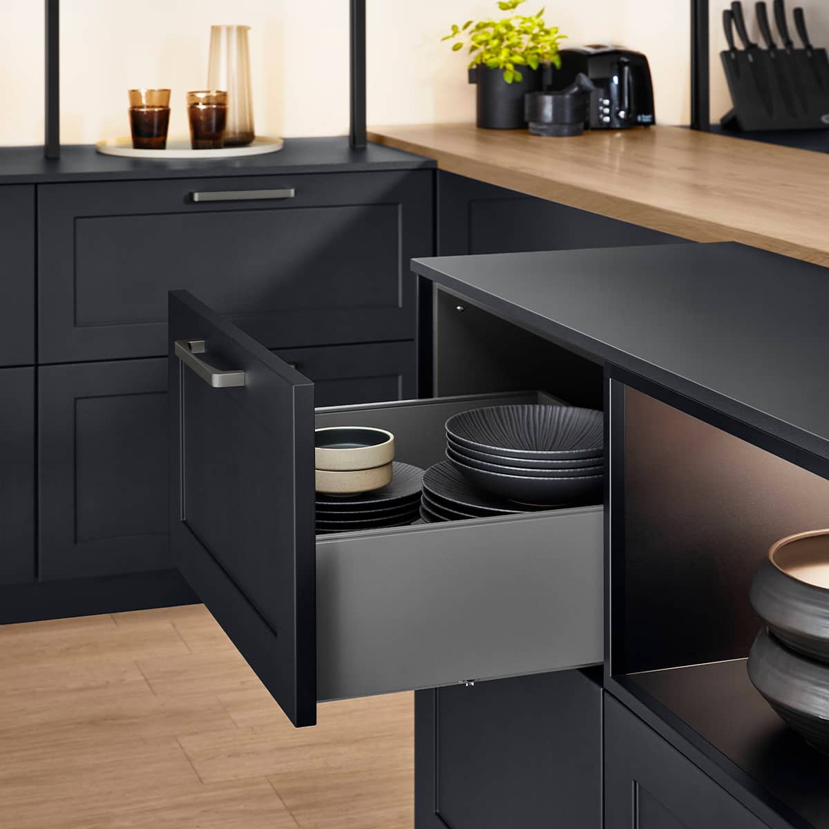Open drawer in a black matt kitchen showing neatly stacked plates and bowls.