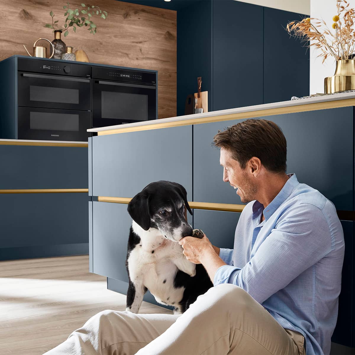 Easytouch 966 Fjord Blue kitchen with Siemens Cooking Appliances Modern Fjord Blue kitchen with gold accents and a person sitting on the floor with a dog.
