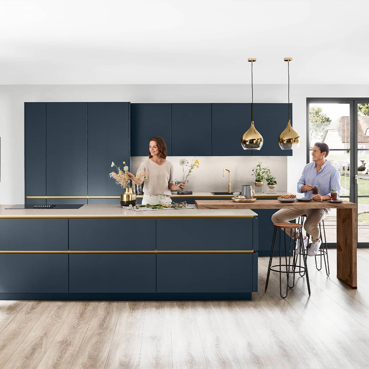Fjord Blue kitchen with gold details, featuring a central island and two people preparing food.