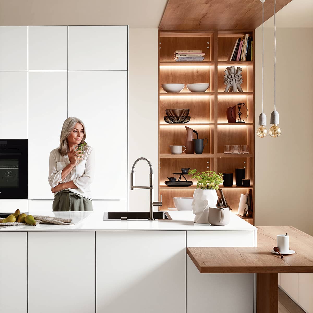 Easytouch 967 Alpine White with human element Alpine White kitchen with warm wood accents, an island with a sink, and illuminated shelving.