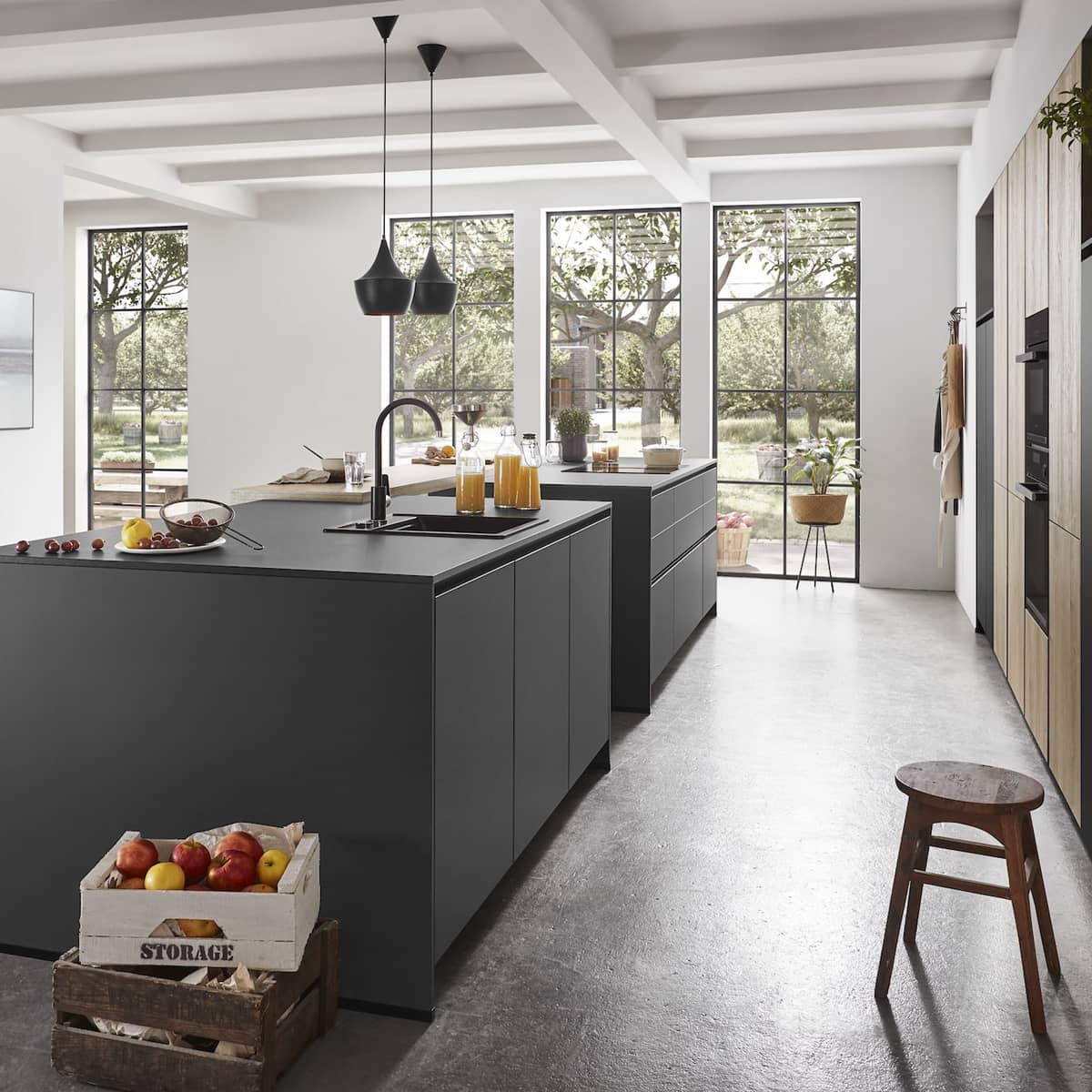Side view of a modern nobilia Natura kitchen featuring dual matte black islands and large floor-to-ceiling windows overlooking a garden.