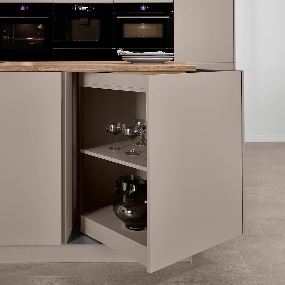 Senso Kitchen 483 - Magic Corner Close-up of a magic corner pull-out kitchen cabinet organizer in a taupe island with wooden countertop and glassware storage.