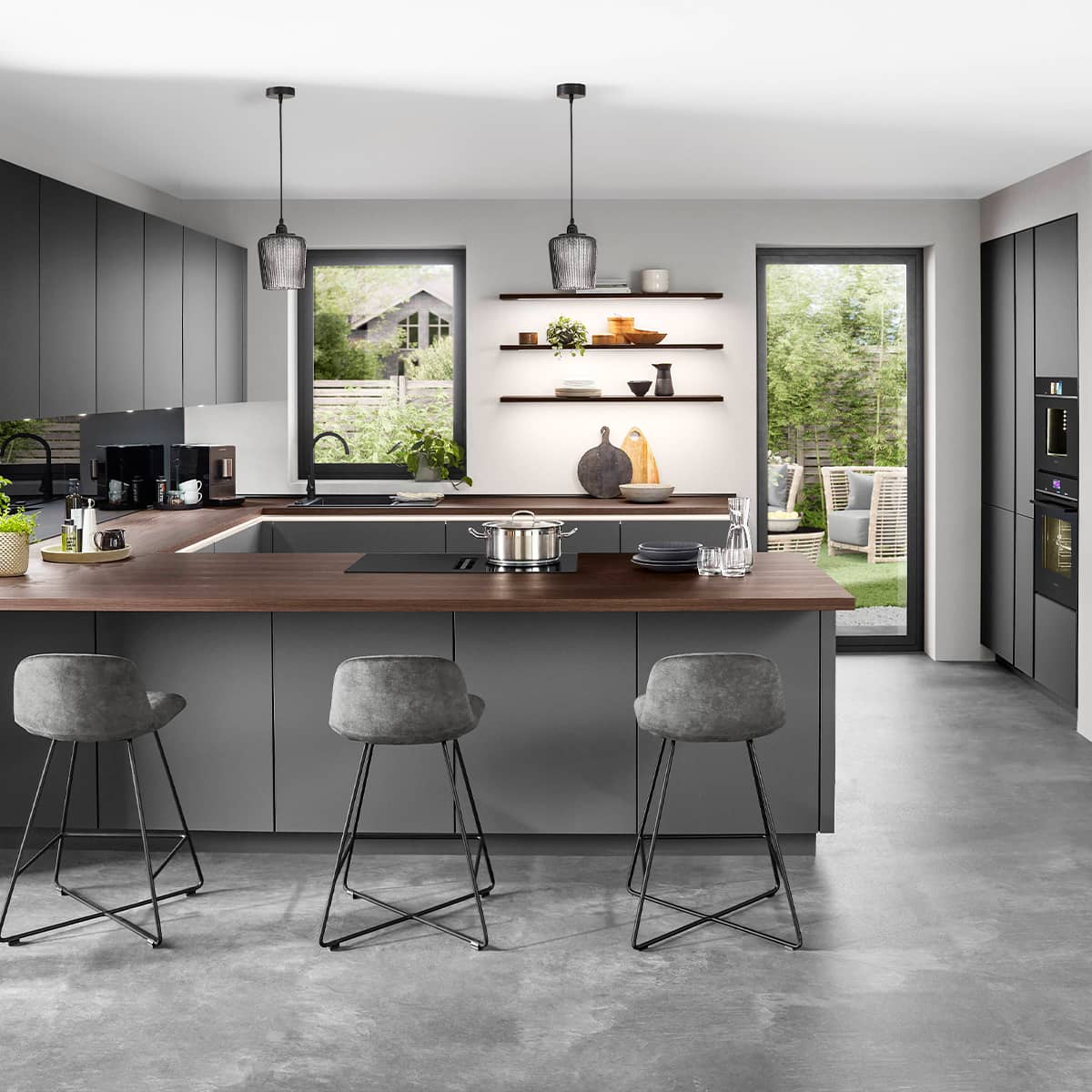 Modern charcoal grey kitchen island with a dark walnut wood countertop, grey swivel bar stools, and minimalist floating shelves.