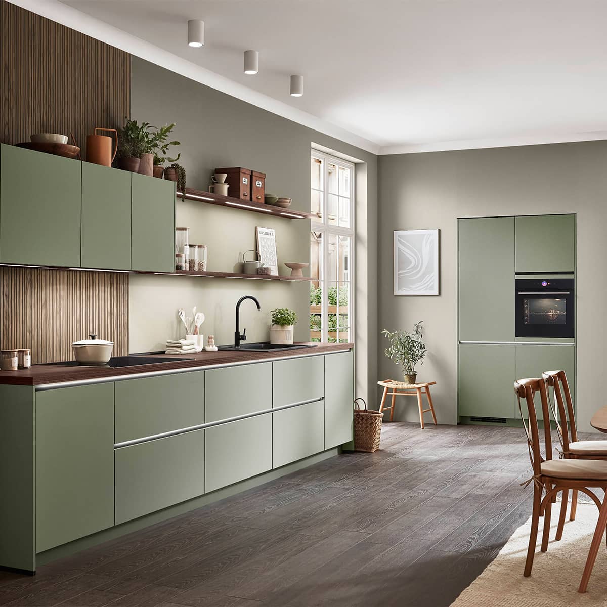 Sage green matte kitchen cabinets featuring dark wood countertops, integrated LED shelf lighting, and a vertical wood slat wall panel.
