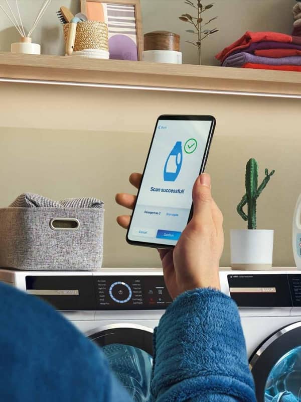 Hand holding a mobile displaying the Home Connect app for Bosch laundry appliances, showcasing smart control features.