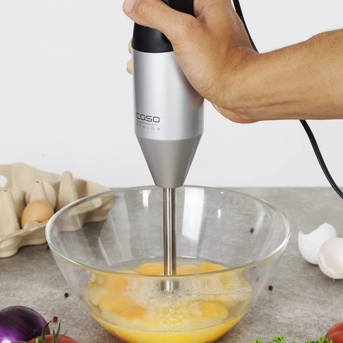 Hand using Caso 3602 Handmixer HB2200 submerged in bowl with broken eggs, mixing ingredients.