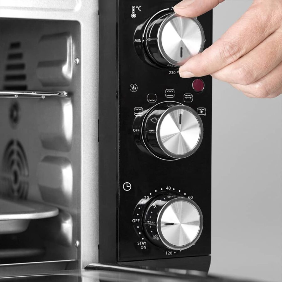 Close-up of hand turning top temperature dial on CASO TO 20 Electronic Oven, showing control knobs.