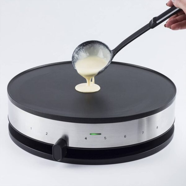 Hand pouring crepe batter with large spoon onto Caso Crepes Maker CM 1300, white background