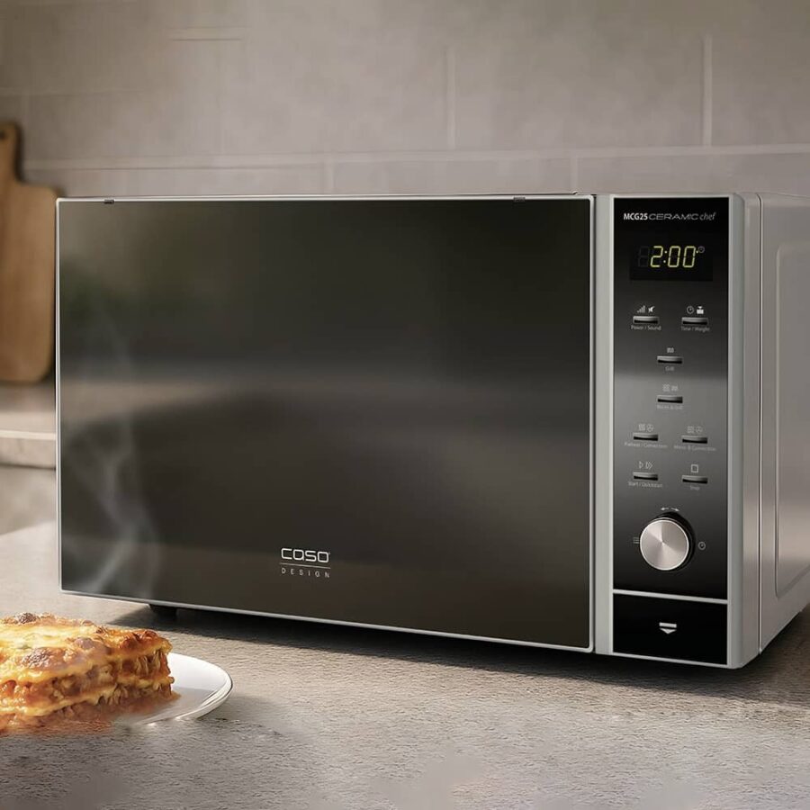 Caso Microwave MCG 25 Chef on kitchen counter with steaming slice of cooked lasagna on plate beside it.
