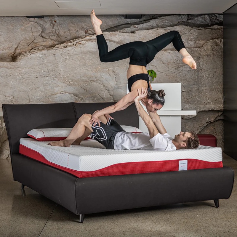 A couple performing an acro-yoga pose on a Dorelan mattress designed for athletes.