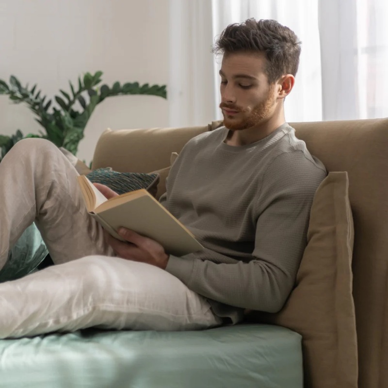 A man unwinds on the bed, reading a book, embracing a moment of digital detox.